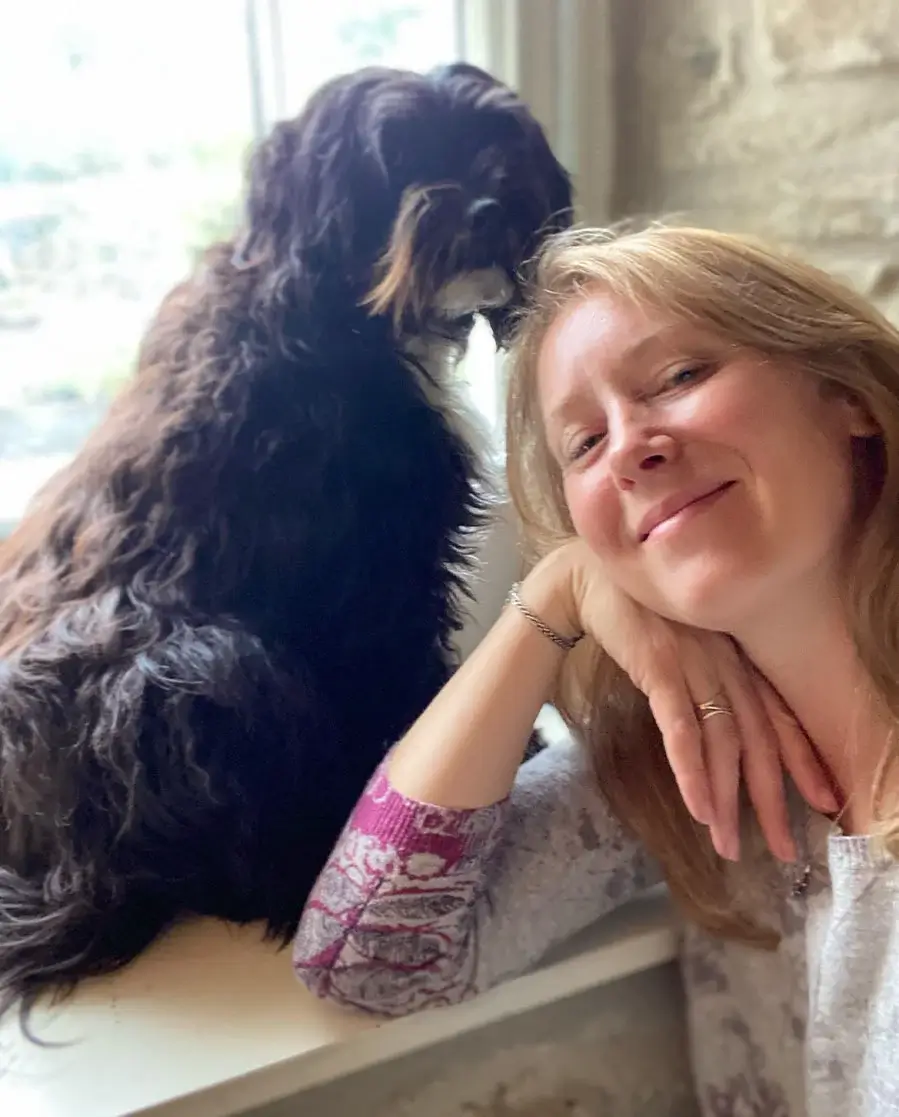 Melanie Phillips smiling next to her Tibetan Terrier, Lily.