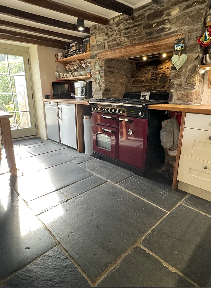 Newly renovated Welsh cottage kitchen featuring exposed stonework, reclaimed slate flooring, and wooden cabinetry.