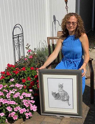 Erika posing proudly with two oil portraits of her family cats, Lucy and Leo, commissioned by Kevin.