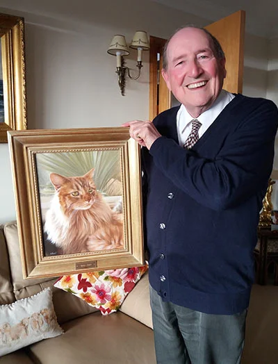 Gordon reacting with joy and surprise as he opens his new cat portrait, held by Kirstie, showcasing their happiness.