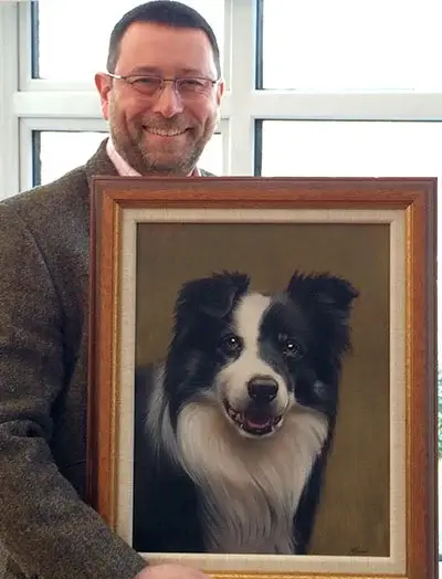A custom pet portrait of Sonny, held by client Gill, who expresses delight on Rob's 50th birthday, feeling like Sonny is 'back again'.